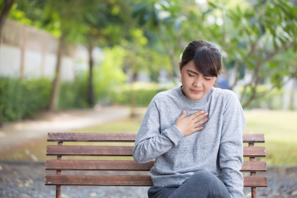 Young woman with acid reflux sitting on park bench touching her chest