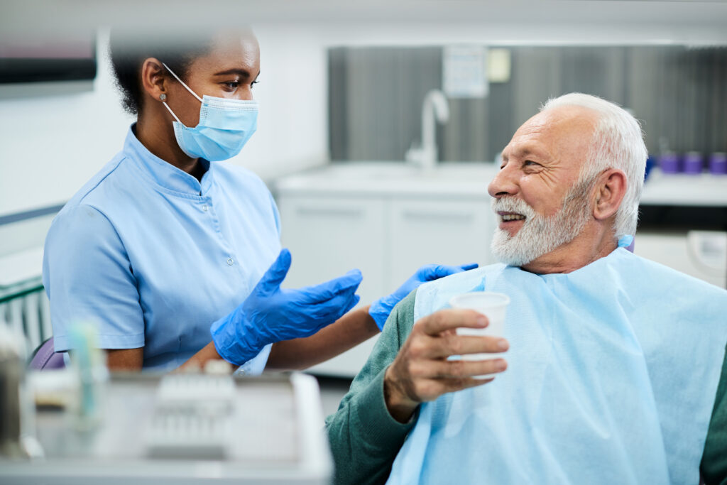 Dental nurse communicating with senior patient during dental procedure at dentist's office.