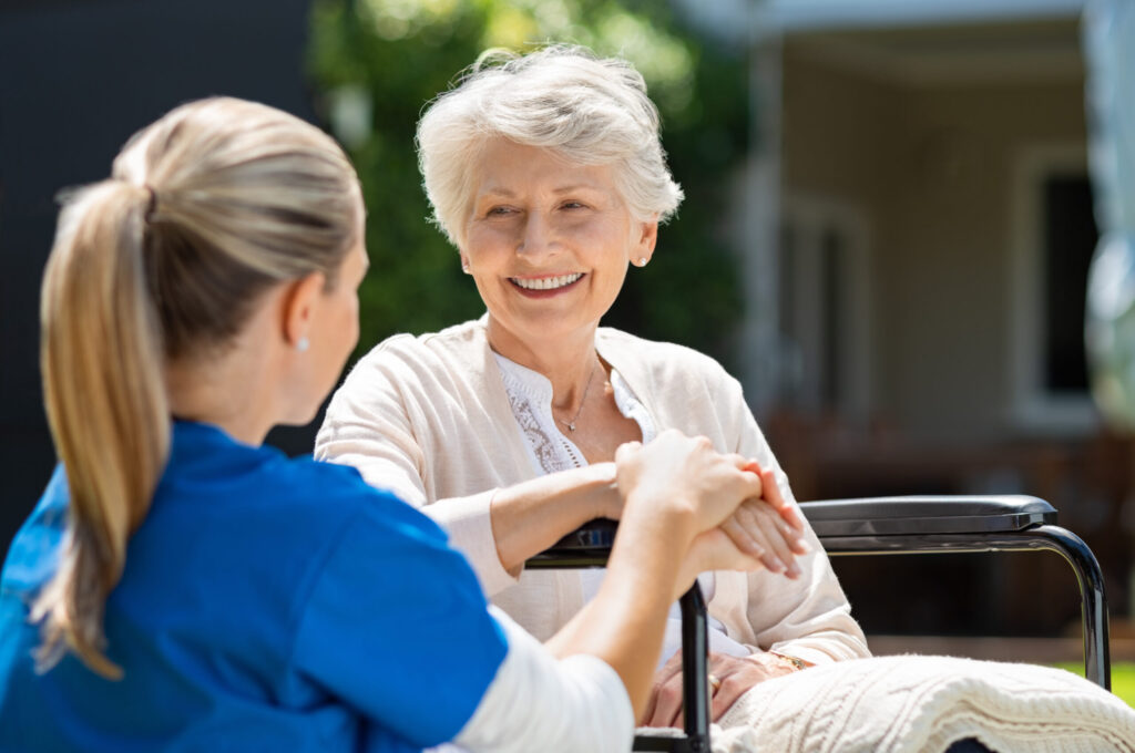 Health care worker assisting smiling older woman in wheelchair