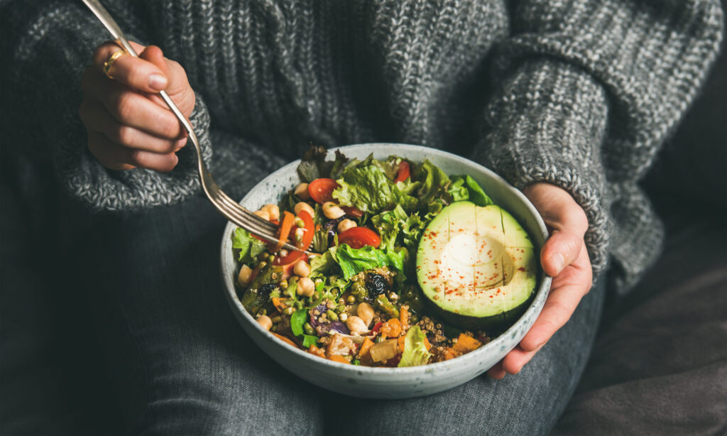 Woman holding a salad bowl full of healthy foods - avocado, lettuce, tomatoes and nuts