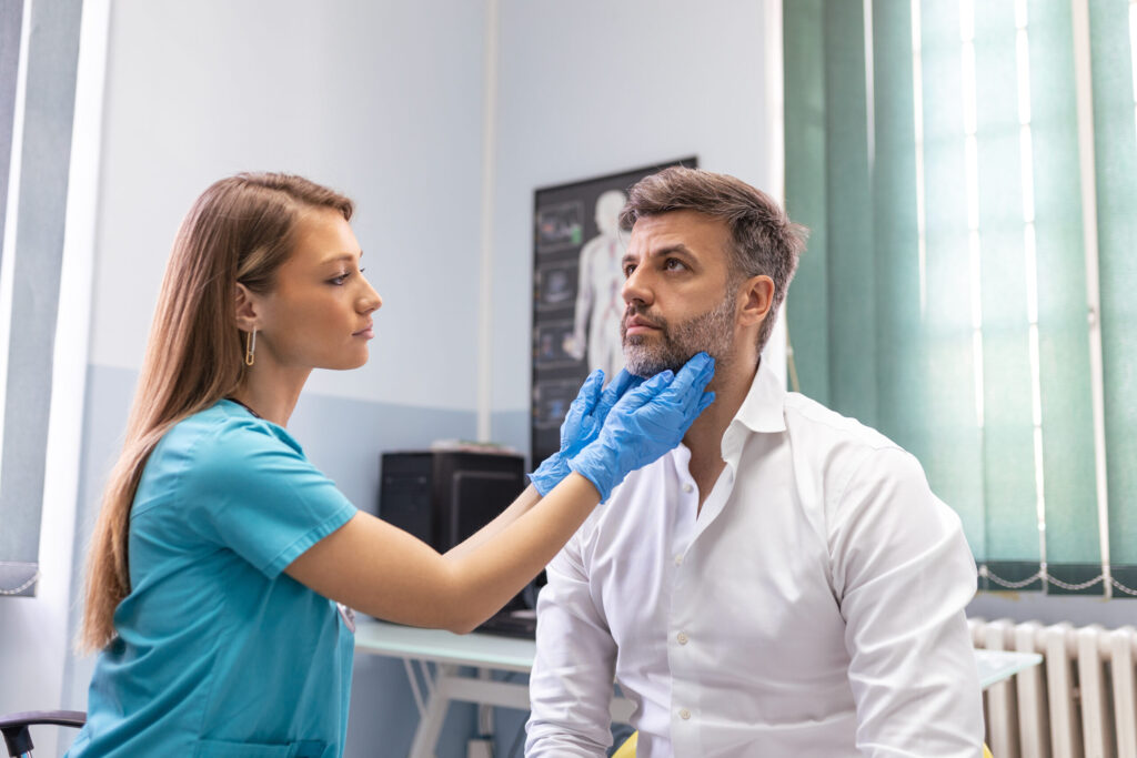 Endocrinologist examining throat of man in clinic.