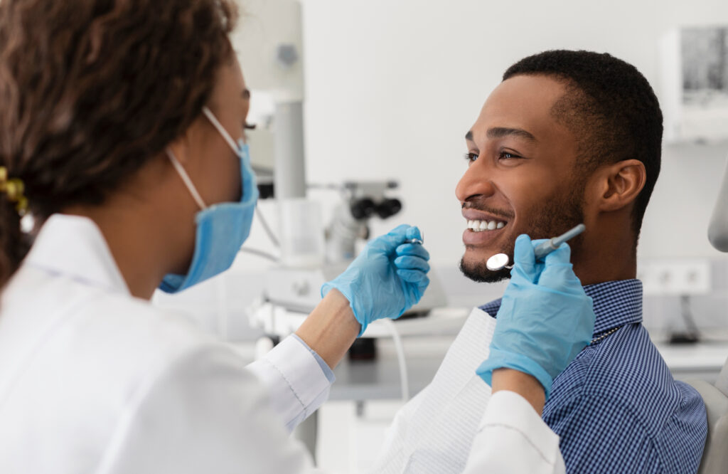 Young man smiling to his female dentist while having treatment at modern clinic