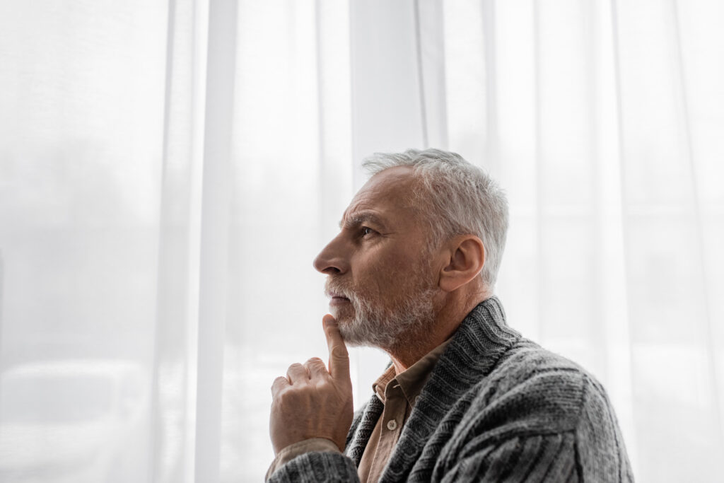 side view of aged man with alzheimer disease looking away near window at home