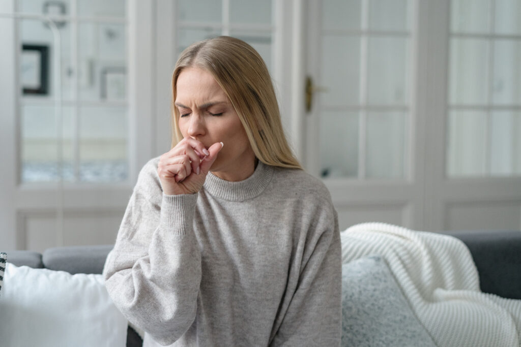 Young woman coughing, sitting on a couch at home
